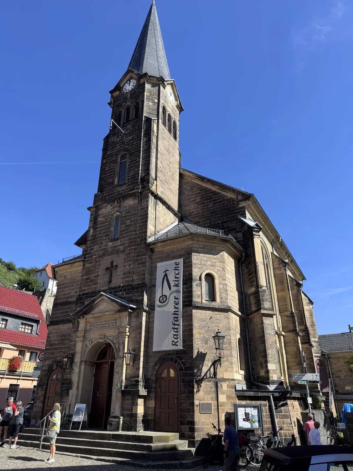 The tall sandstone church of Stadt Wehlen against a deep blue sky, with a banner reading Radfahrerkirche hanging beside its door.